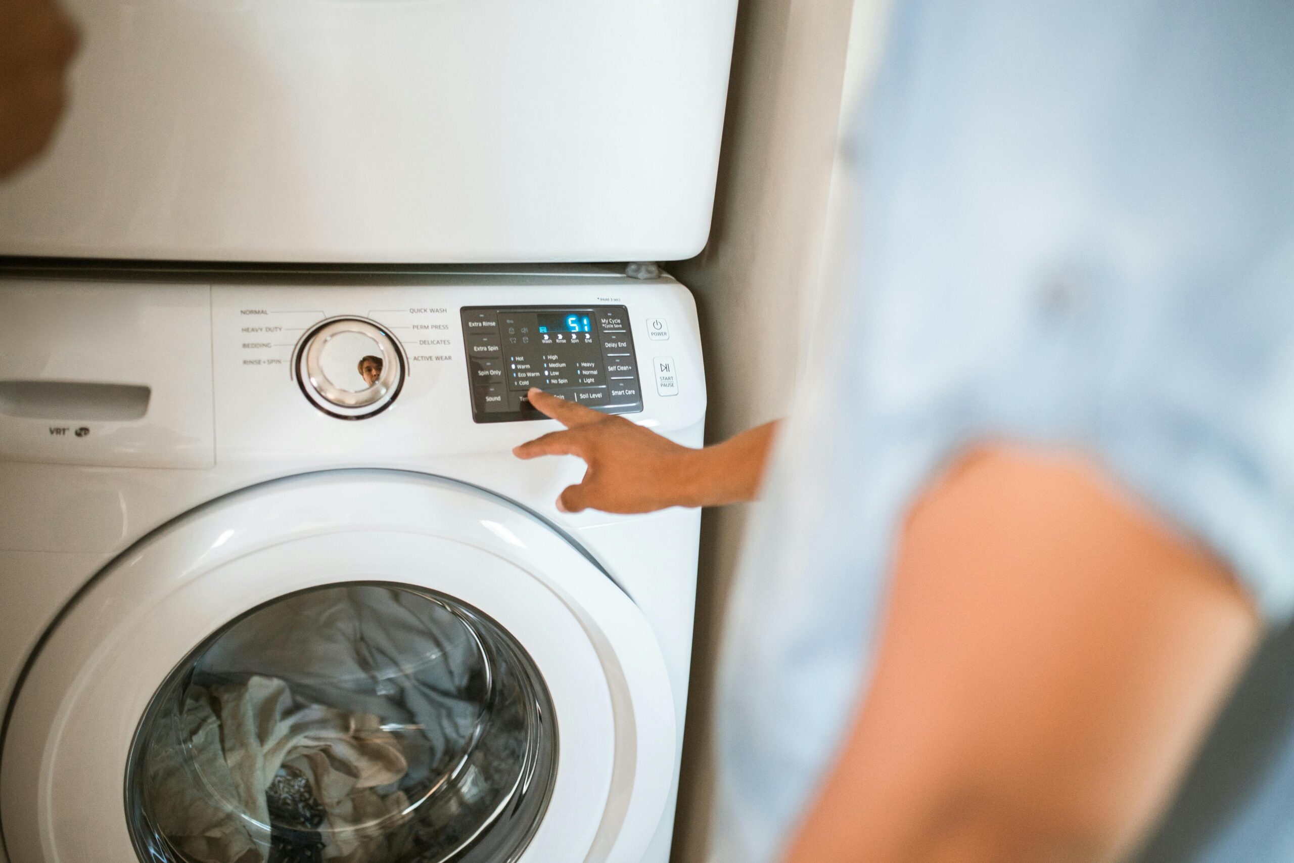 Hand selecting laundry options on a digital washing machine control panel indoors.